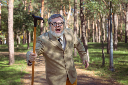 Funny old man with a stick. An elderly man with a walking stick with a funny face. The man has a funny face with a beard.の写真素材