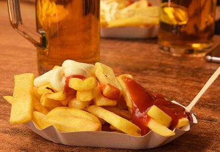 Fast food outdoors - a plate of french fries with tomato sauce and beerの写真素材