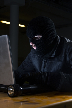 masked hacker sitting behind compuiterの写真素材