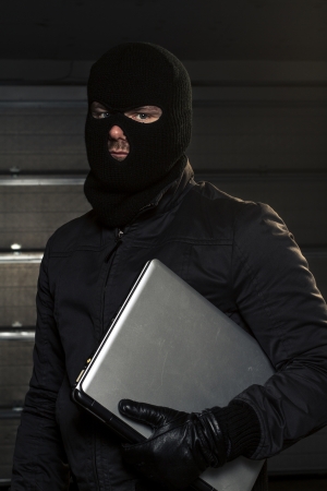masked hacker holding computerの写真素材