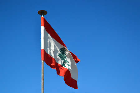 The Lebanese flag consists of two horizontal red stripes on the edge of the flag. Between them is a white stripe with a silhouette of green cedar, with a blue sky in the background.の写真素材