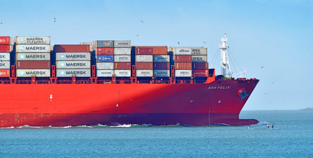 Container ship loaded with cargo, close-up view, at the tip of the ship people on a paddleboard....