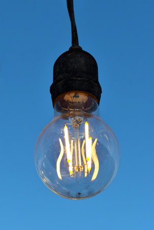 Close-up of a lit light bulb, filaments in the middle of a light bulb, blue background.