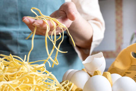 Homemade noodles, with eggs, italian pasta, fettuccini, woman making pasta in the kitchen. Italian food.の写真素材