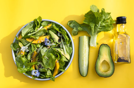Organic Healthy Salad with mango and avocado on yeliow Background. Top View.