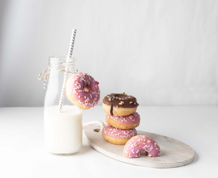 Glazed donuts with milk in a glass bottle on a light background.