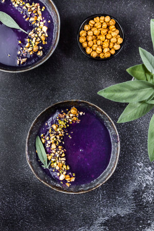 Food photo with bright red cabbage cream soup. With chickpeas and sage leaves are laying nearby....