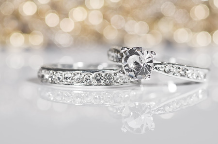 Silver Rings with diamonds on the white surface with golden reflections in the background.の写真素材
