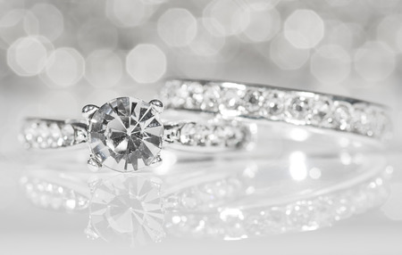 Silver rings with diamonds on the white surface with reflections in the background.の写真素材