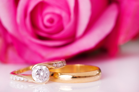 Rings of gold on a white surface with a rose in the background.の写真素材