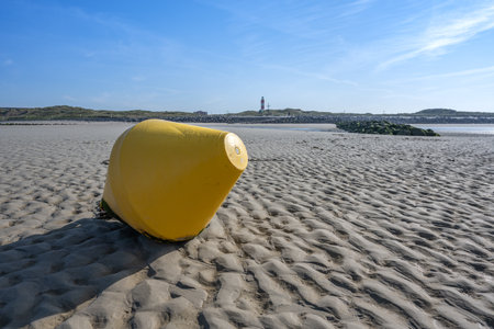 yellow buoy with lighthouse in the background at the beach of Berck in northern france. Sand is throwing shadows.の写真素材