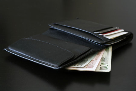 Euro bills coming out of a black wallet.