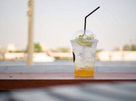 A fresh lemon-soda with lemon sliced drink in a plastic cup is placed on a wooden table. The...