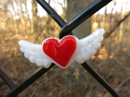 Glass red heart with wings magnet centered on chain link fence.の写真素材