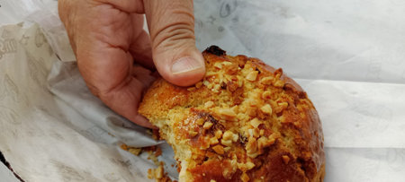 A man's hand holds a piece of cake with nuts and raisins.
