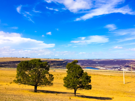 Dry hot desert with trees, deep open coal mine exploration and cloudy blue sky in the rural countrysideの写真素材
