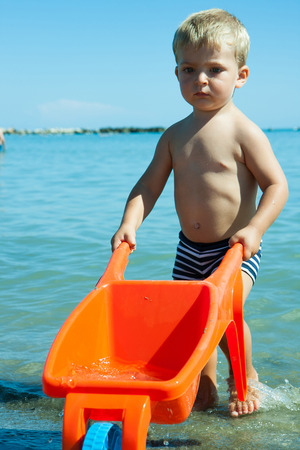 child with wheelbarrow carries water from the seaの写真素材