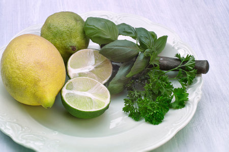 Lemons and a halved lemon with basil and parsley on a light porcelain plateの写真素材