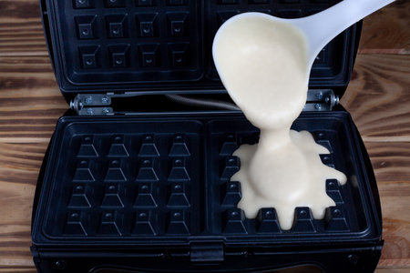 Waffle iron in the kitchen. Preparing homemade waffles, pouring a dough. Belgian viennese wafflesの写真素材