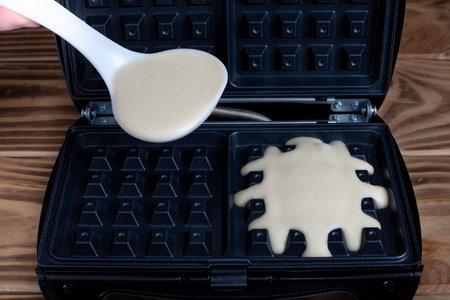 Waffle iron in the kitchen. Preparing homemade waffles, pouring a dough. Belgian viennese wafflesの写真素材