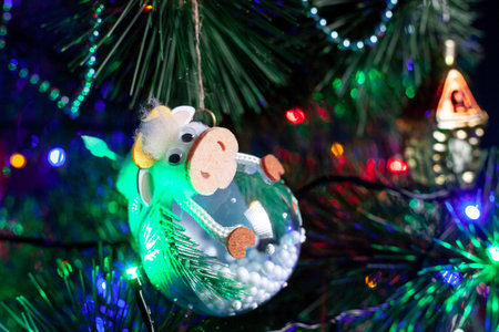 Christmas decoration, glass ball with cow on a green Christmas tree branch. christmas garland on tree. Shallow depth of field ball with golden ornament. New year backgroundの写真素材