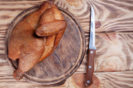 smoked half chicken on wooden cutting board with sharp knife. fried roasted chicken on wooden table. top viewの写真素材