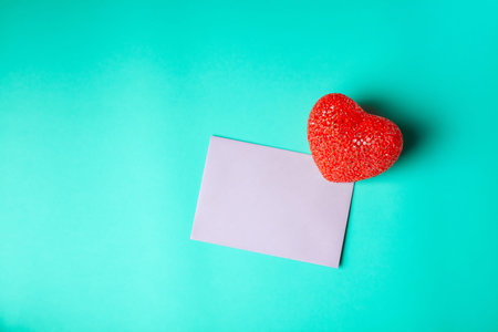Blank pink greeting card with red heart on cyan background with copy space