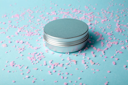 Metal jar of cream on blue background with pink salt. Aluminum pot for natural cosmetic product....