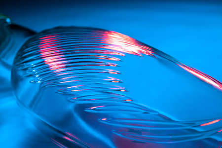 Abstract glass bottle background. Texture of wavy glass illuminated with multi-colored light. Pink and blue stains. Close up. Flares on glassの写真素材