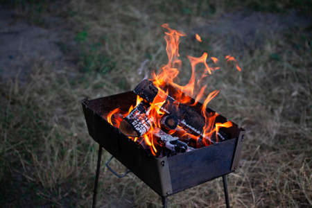A small folding portable brazier filled with burning wood. Cooking on the grill. Safe fire in nature. firewood. Flames in brazier.の写真素材