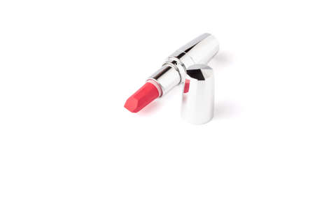 Red lipstick lies on the surface isolated on white background with copy space. Red lipstick in metallic shining case close up. makeup product macroの写真素材