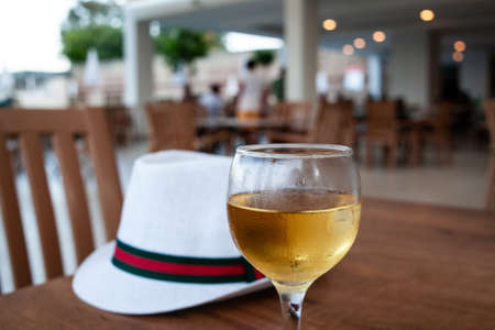 A glass of wine and white hat on table. Condensation on the glass of refreshing wine. Cool drink in open-air restaurant.の写真素材