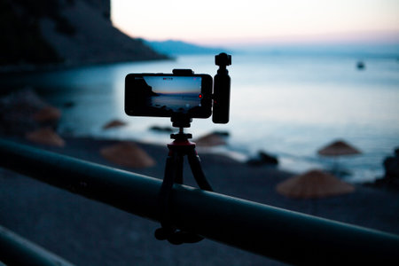 mobile phone with portable camera mounted on a tripod filming sunrise over sea bay. Taking video...