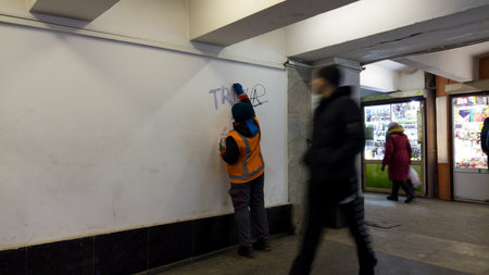 Removing graffiti from vandals in underground pass. employee of the city, wearing a orange uniform, cleans wall from graffiti and writing, with a liquid solvent. Kharkiv, Ukraine - December 27, 2022のeditorial素材