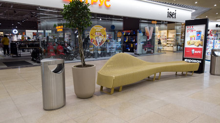 Wooden bench and trash can in the shopping mall. Recreation area in the shopping center with wooden benches and artificial pond with fountains. Kharkiv, Ukraine - December 18, 2021のeditorial素材