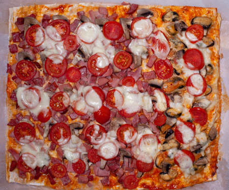 Homemade pizza on baking sheet with ham, mushrooms, mozzarella cheese, cherry tomatoes. Italian food. Baked pizza top view.の写真素材