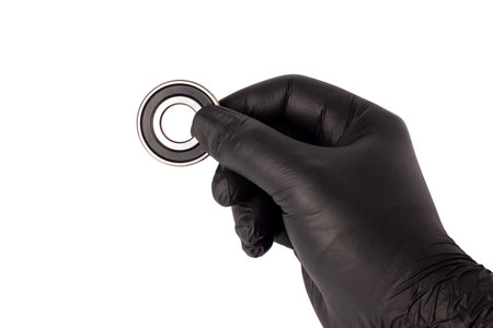 Male hand in nitrile glove holding metal roller bearing. Ball bearing isolated. Super Precision Ball...