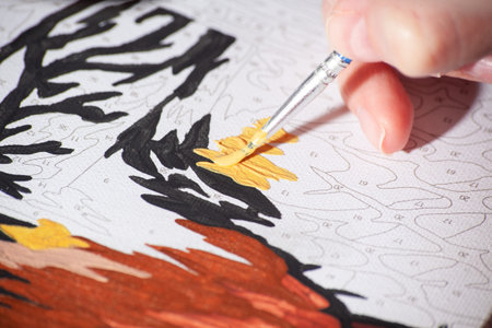 Paint by numbers close up. Female hand with brush drawing. Active leisure at home, creative hobby...
