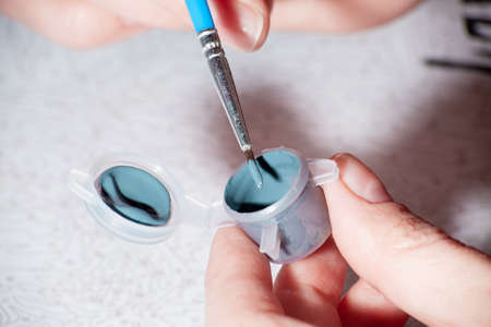 Acrylic paint jar with paintbrush for paint by numbers close up. Female hand with brush. Leisure at home, creative hobby. Numbered paints. painting by numbers process. Selective focus on paintbrush.の写真素材