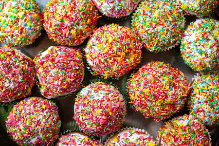 Homemade cupcakes decorated sugar sprinkles top view. Group of homemade vanilla muffins white glazed multicolored decoration. Sweet cake background.の写真素材