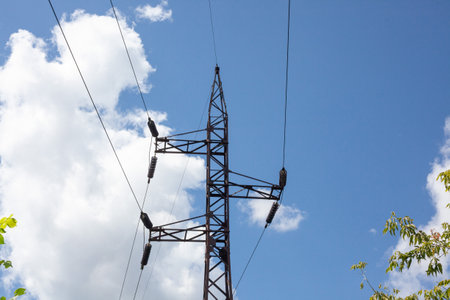 High voltage electric pole set as one of many on the entire length of the eclectic line. Metal electric pole against blue sky with white cloudsの写真素材