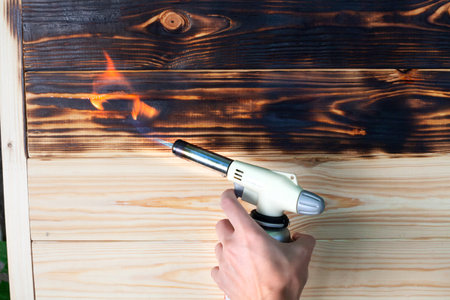 Burning wooden board by gas-burner. Brushing with a gas burner at home. Treating the soft part of...