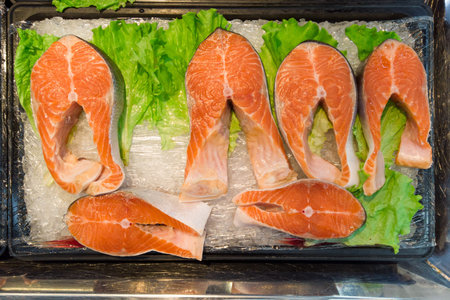 Various fresh fish fillets and steaks on ice at a seafood market counter with leafy greens