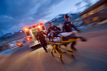 Two paramedics unload a stretcher from an ambulance on a street as dusk falls. The scene shows quick action in an urgent situation to assist a patient.の素材