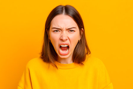A young woman with a fierce expression shouts passionately, showing her emotions in a vibrant yellow setting that enhances her powerful presence.の素材