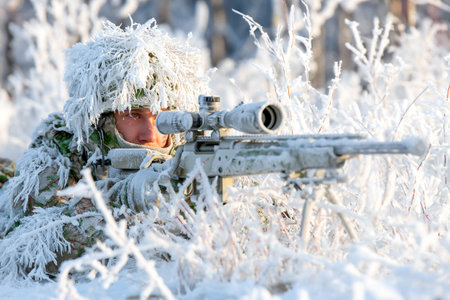 A sniper is camouflaged in snow-covered terrain, focused intently through the scope of his rifle. The winter landscape is frosted and quiet, enhancing the stealth.の素材