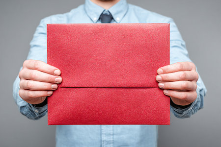 A person holds a bright red envelope in front of a gray background, showing the delivery mail style. The focus is on the envelope, creating a sense of anticipation.の素材