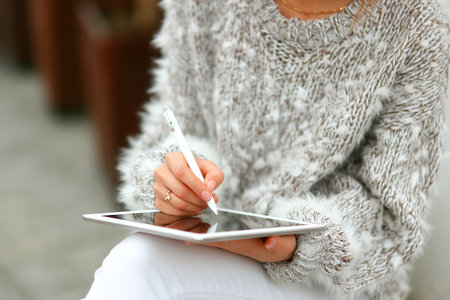 A person is seated outside, using a stylus to create art on a tablet. The cozy atmosphere features soft textures and a lush environment, highlighting creativity.の素材
