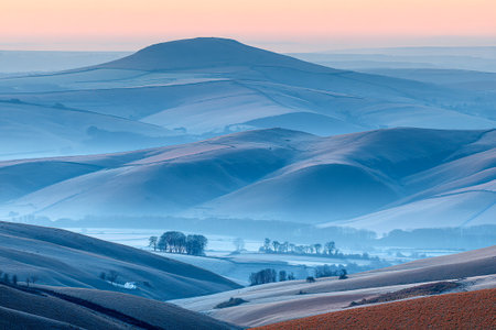 Soft morning light illuminates the rolling farmland, revealing gentle hills and tree lines. A serene landscape invites tranquility as mist blankets the valleys below.の素材