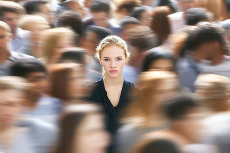 A young woman stands out in a crowd, appearing uneasy amidst the bustling gathering. The lively atmosphere highlights her feelings of social discomfort.の素材